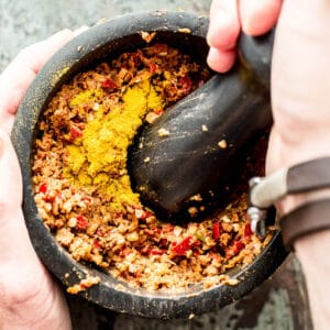 pounding massaman curry paste in black pestle and mortar.