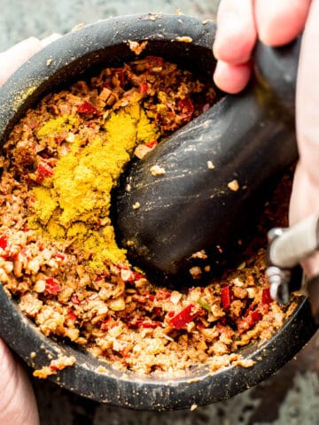 pounding massaman curry paste in black pestle and mortar.