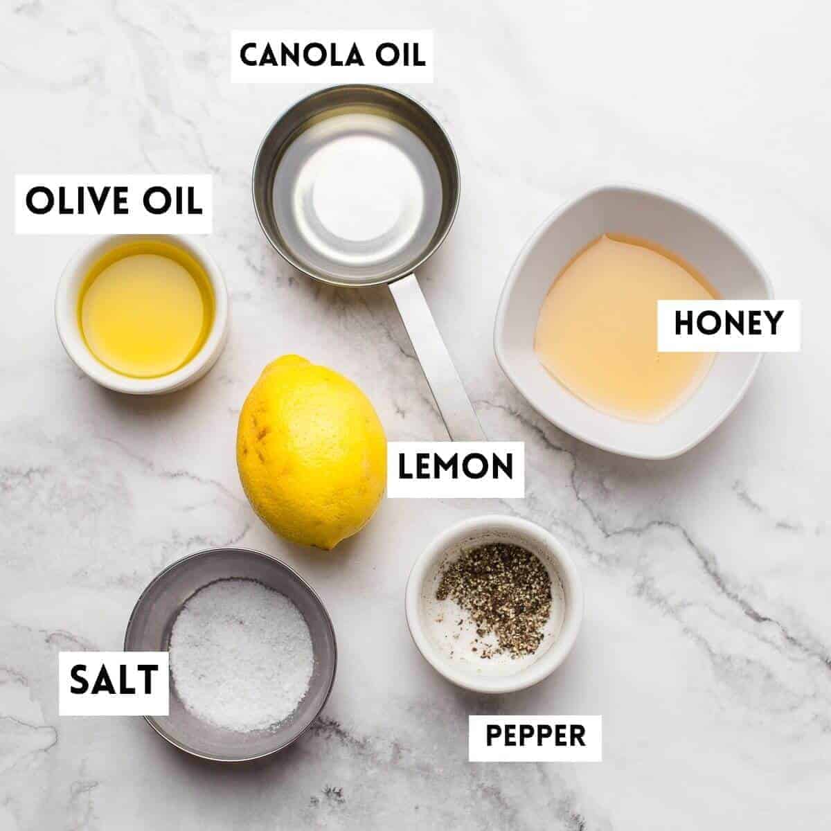 ingredients to make honey lemon dressing. hoey,lemon, olive oil,salt,pepper,canola oil on marble background