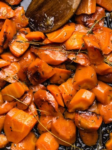 hooney roasted orange carrots with thyme leaves in black oven tray