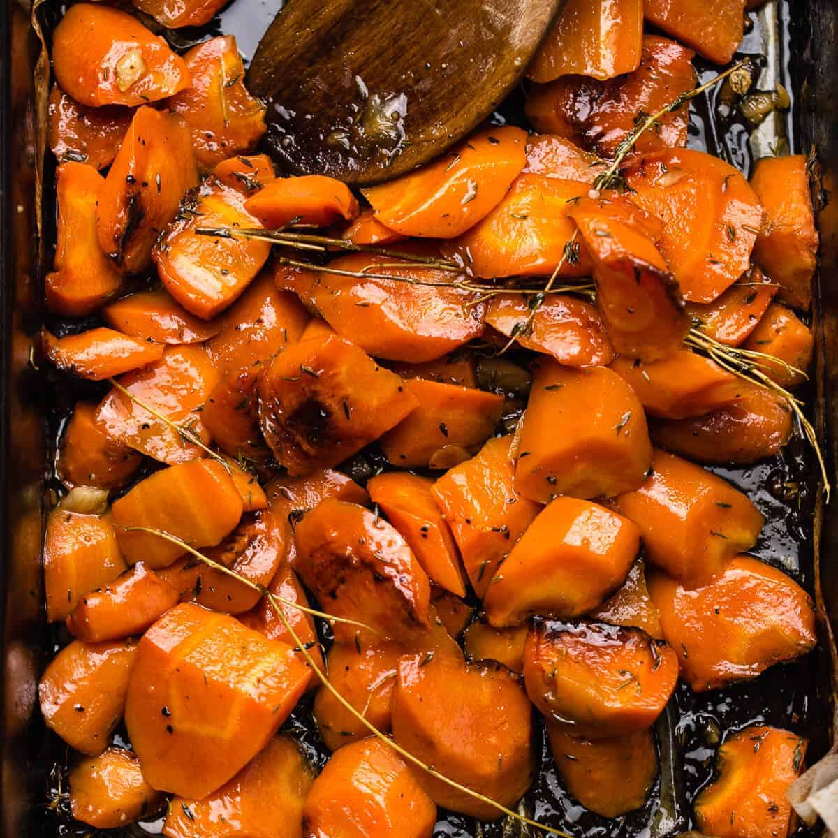 honey roasted orange carrots with thyme leaves in black oven tray