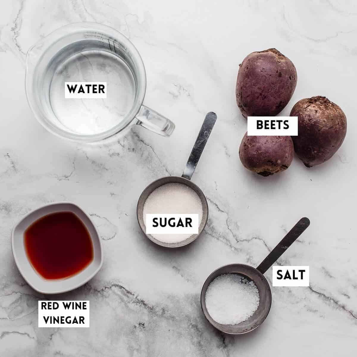 Ingredients for boiling beets on a marble background, beets, water, sugar, salt, and vinegar.
