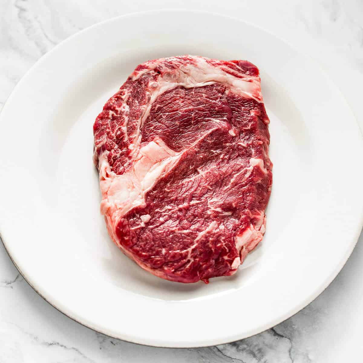 Raw USDA prime ribeye steak on a white plate.