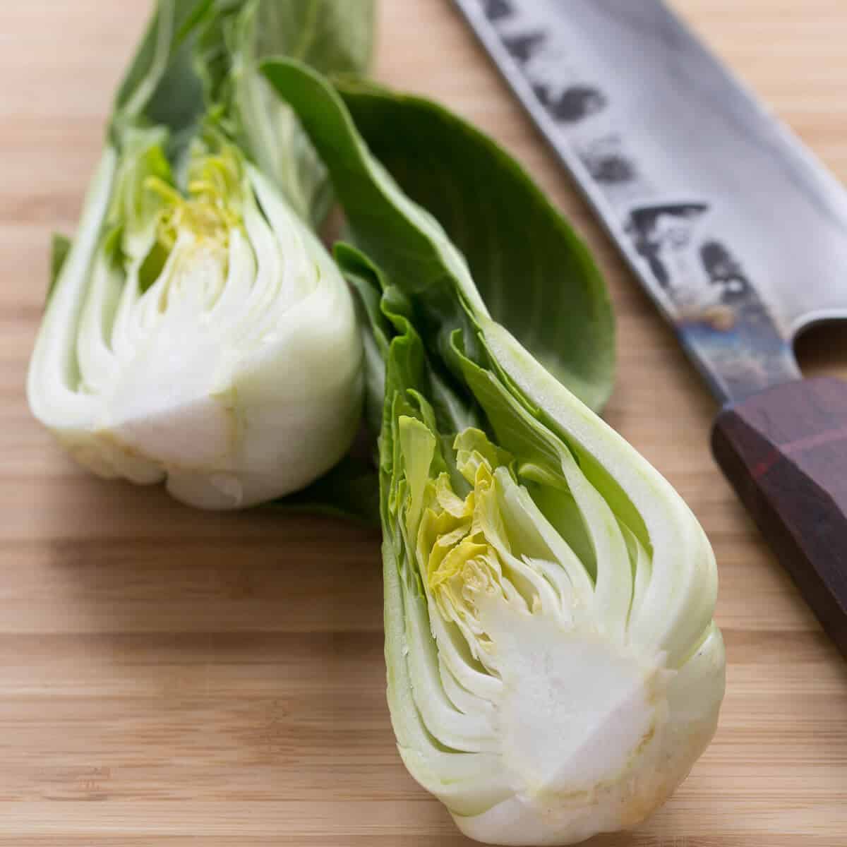 cut bok choy on wooden board next to a knife.