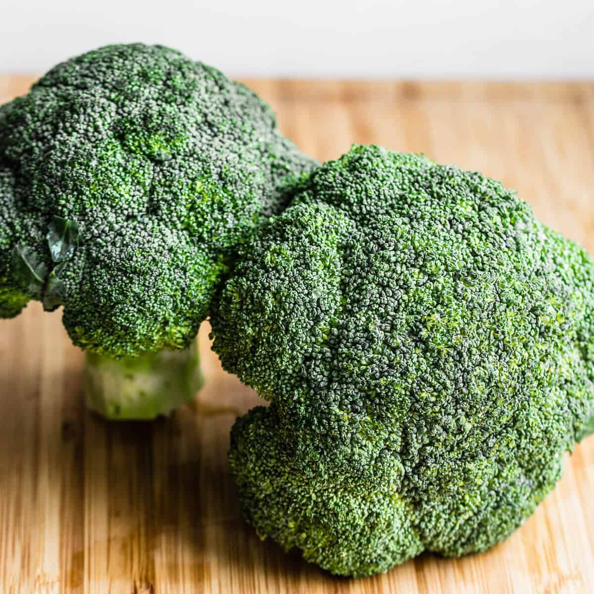 two heads of broccoli on wooden board