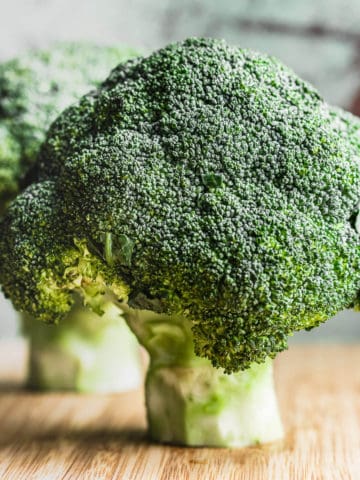 two heads of broccoli on wooden board