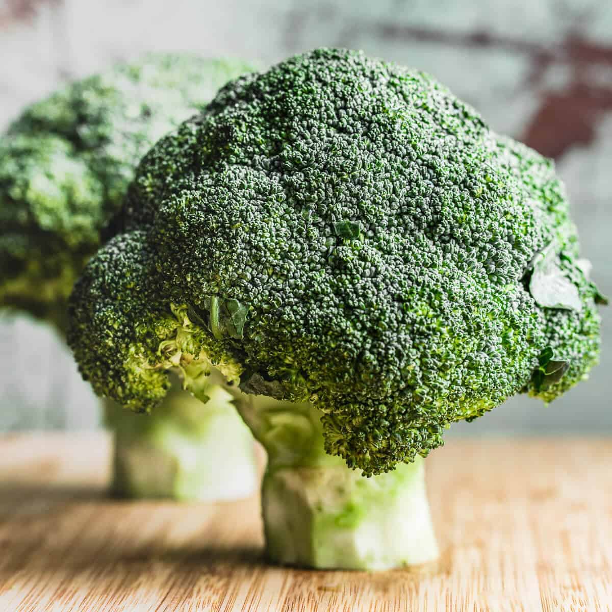 two heads of broccoli on wooden board