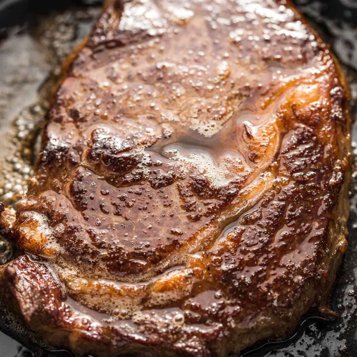 Ribeye beef steak searing in a pan with butter.