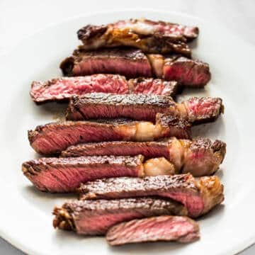 medium rare ribeye steak cooked in a cast iron skillet sliced on a white plate