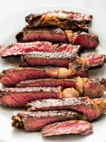 medium rare ribeye steak cooked in a cast iron skillet sliced on a white plate