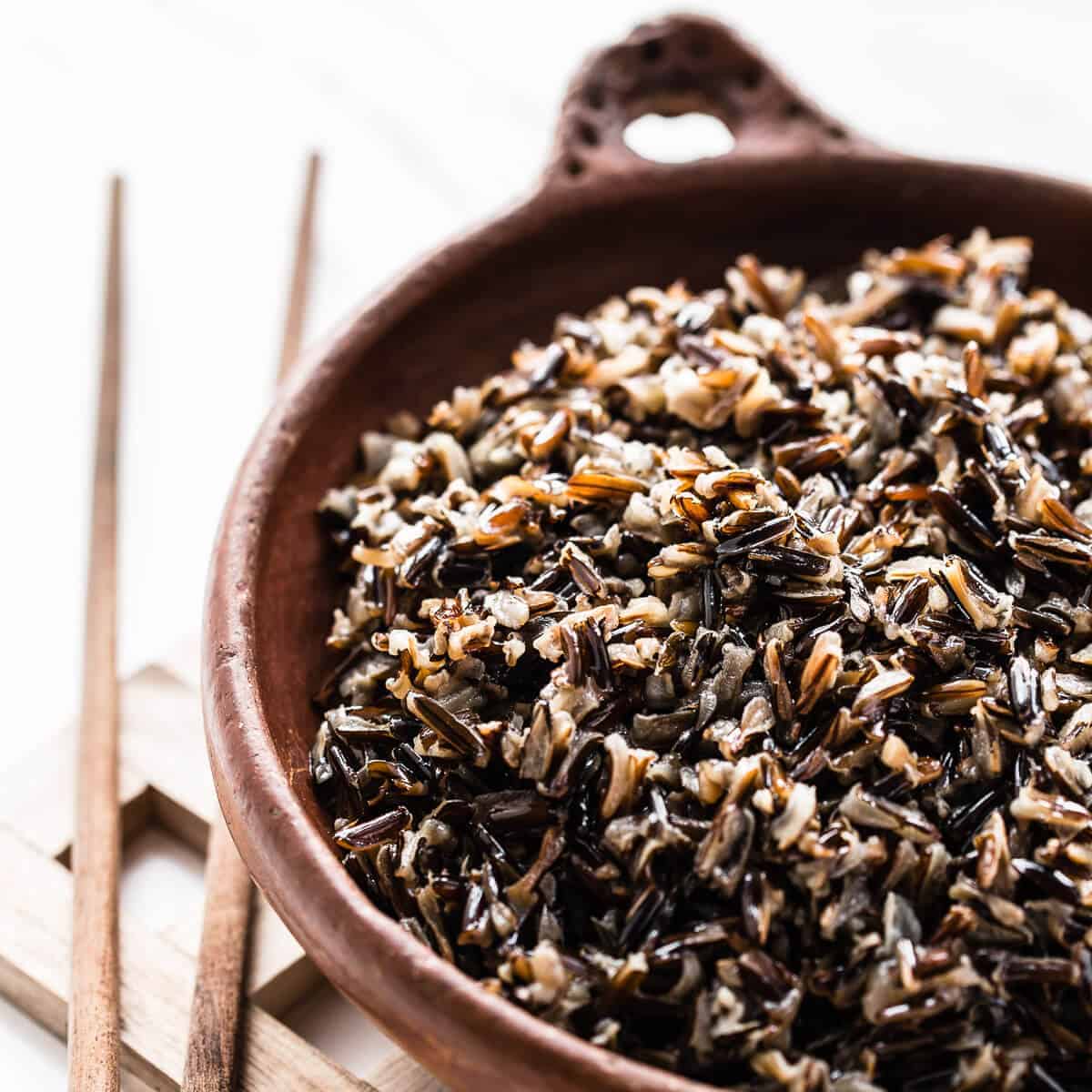 Cooked wild rice in a brown bowl on a wooden table.