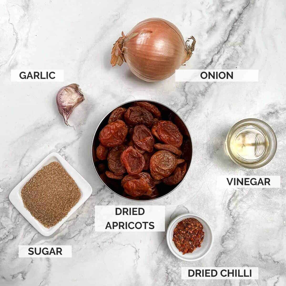 Ingredients for making apricot chilli chutney on a marble background.