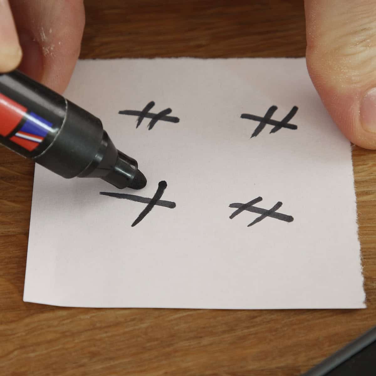 Hands draw cross symbols on white paper using a black marker.
