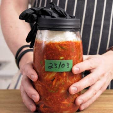 Glass jar with kimchi covered with a black rubber glove.