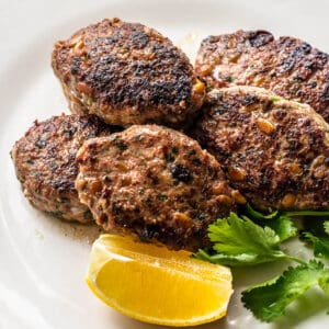 lamb koftas on white plate with lemon and cilantro