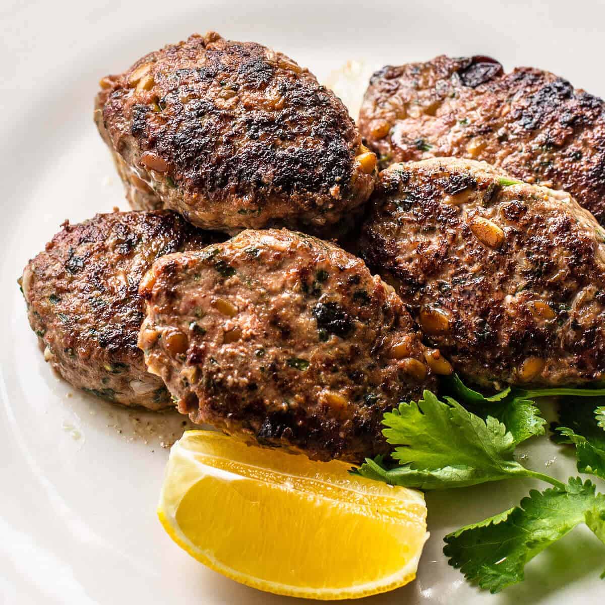 authentic lamb koftas on a white plate with lemon wedge and cilantro