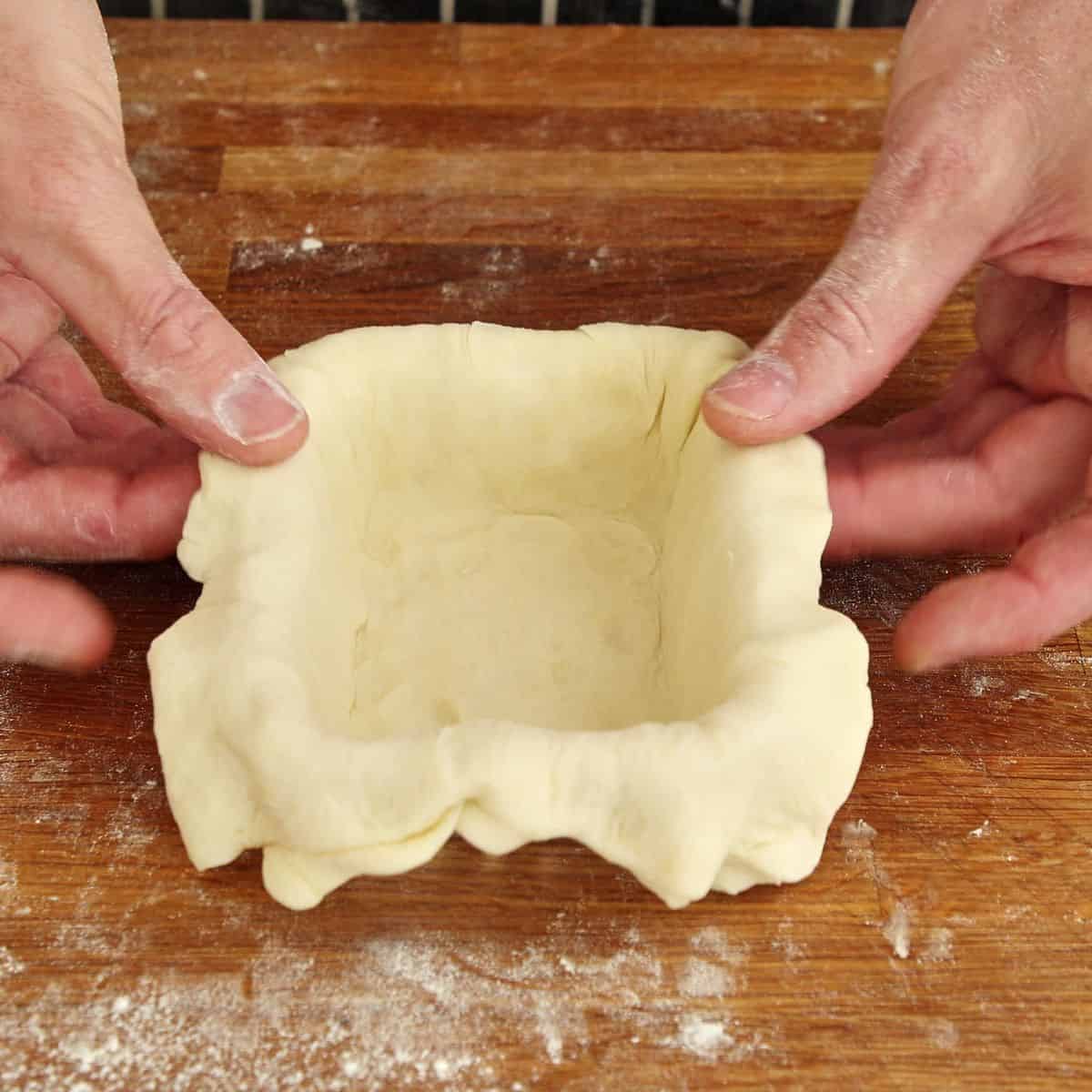 Hands lining a pie tin with pastry.