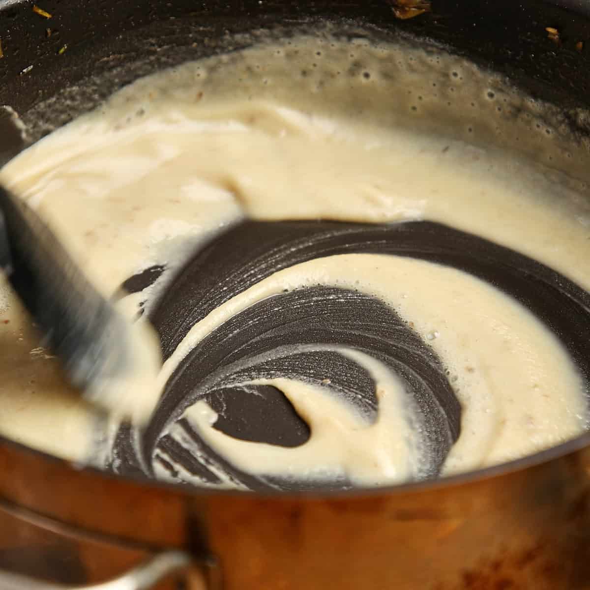 A blonde roux being whisked in a dark saucepan.