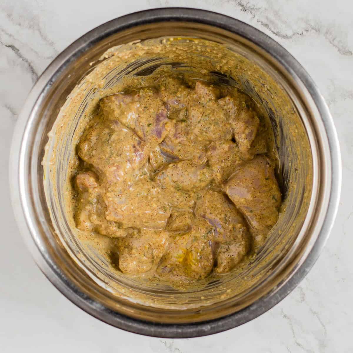 Chicken mixed with marinade in a steel mixing bowl.