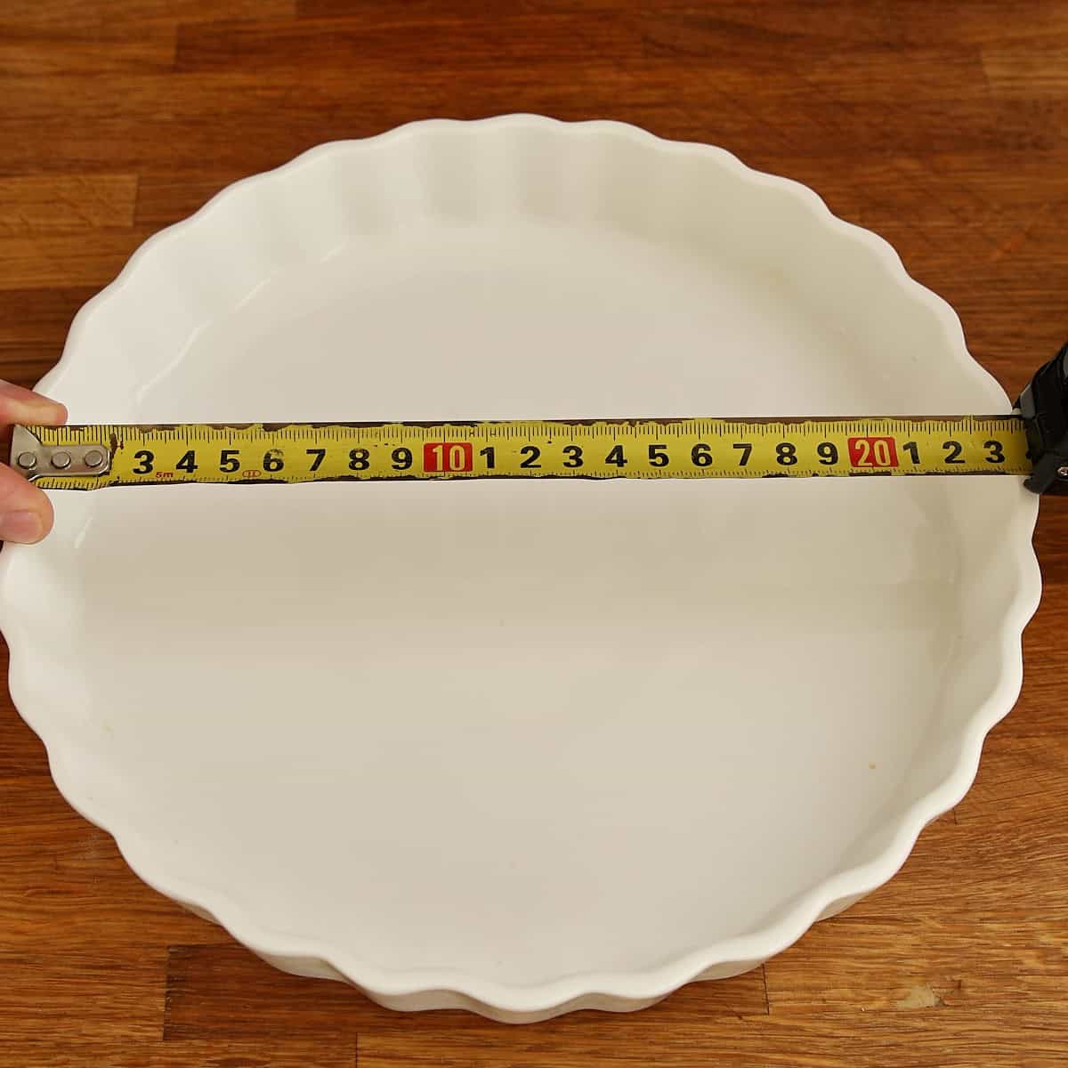 Tart dish being measured across its diameter with a tape measure.