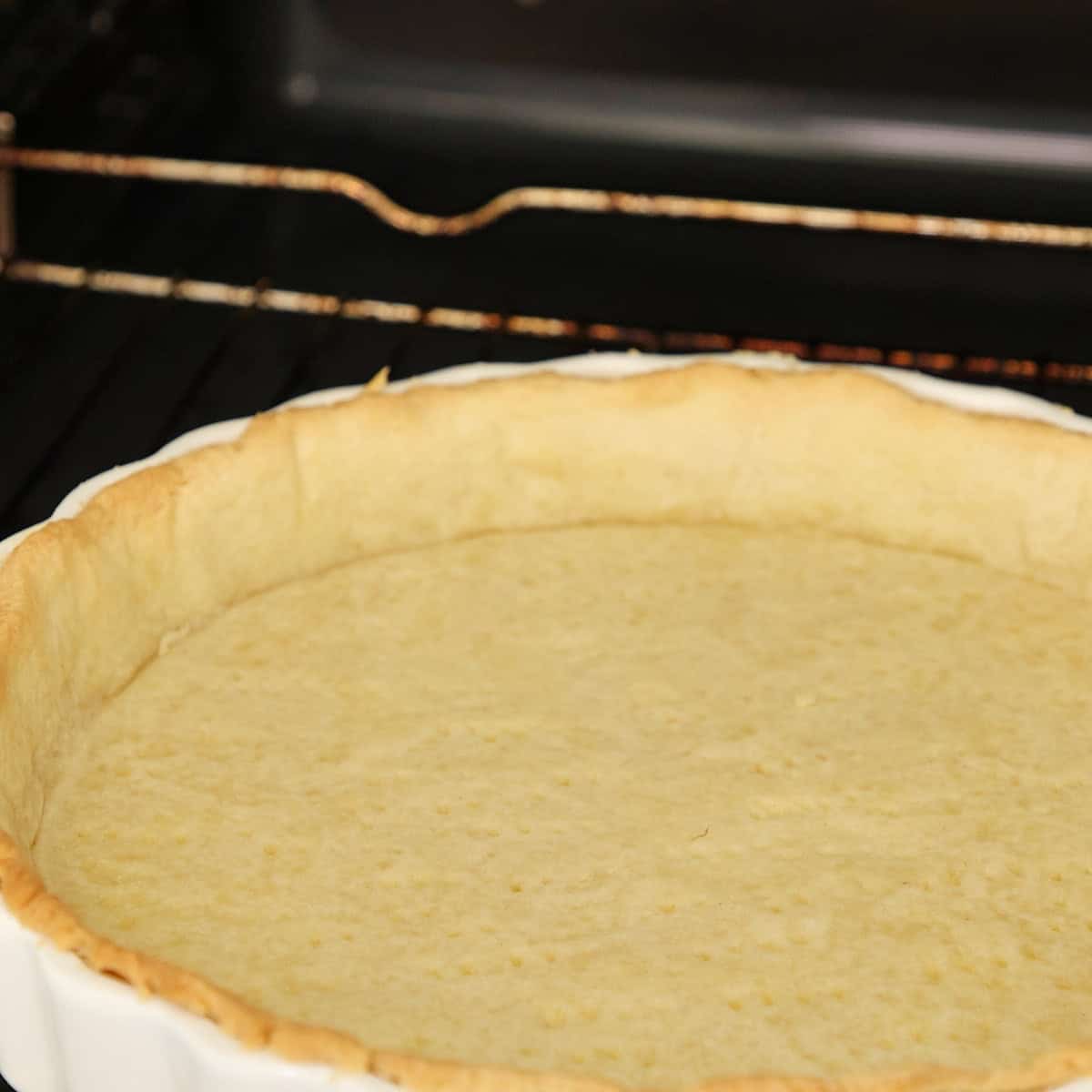 Baked custard tart in white ceramic dish with pastry crust inside oven.