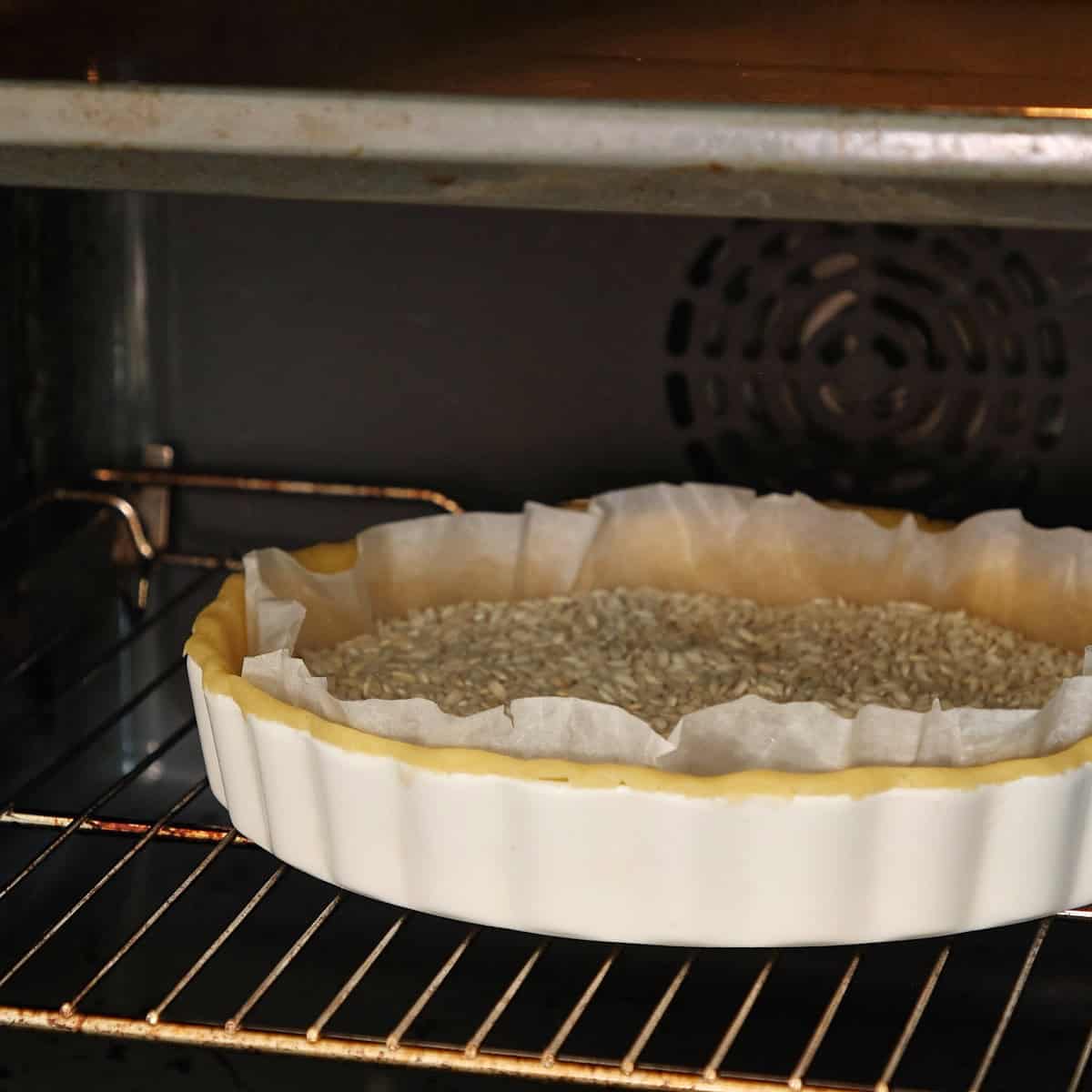 Blind-baked pastry shell lined with parchment, filled with custard and cinnamon-dusted breadcrumb mixture.