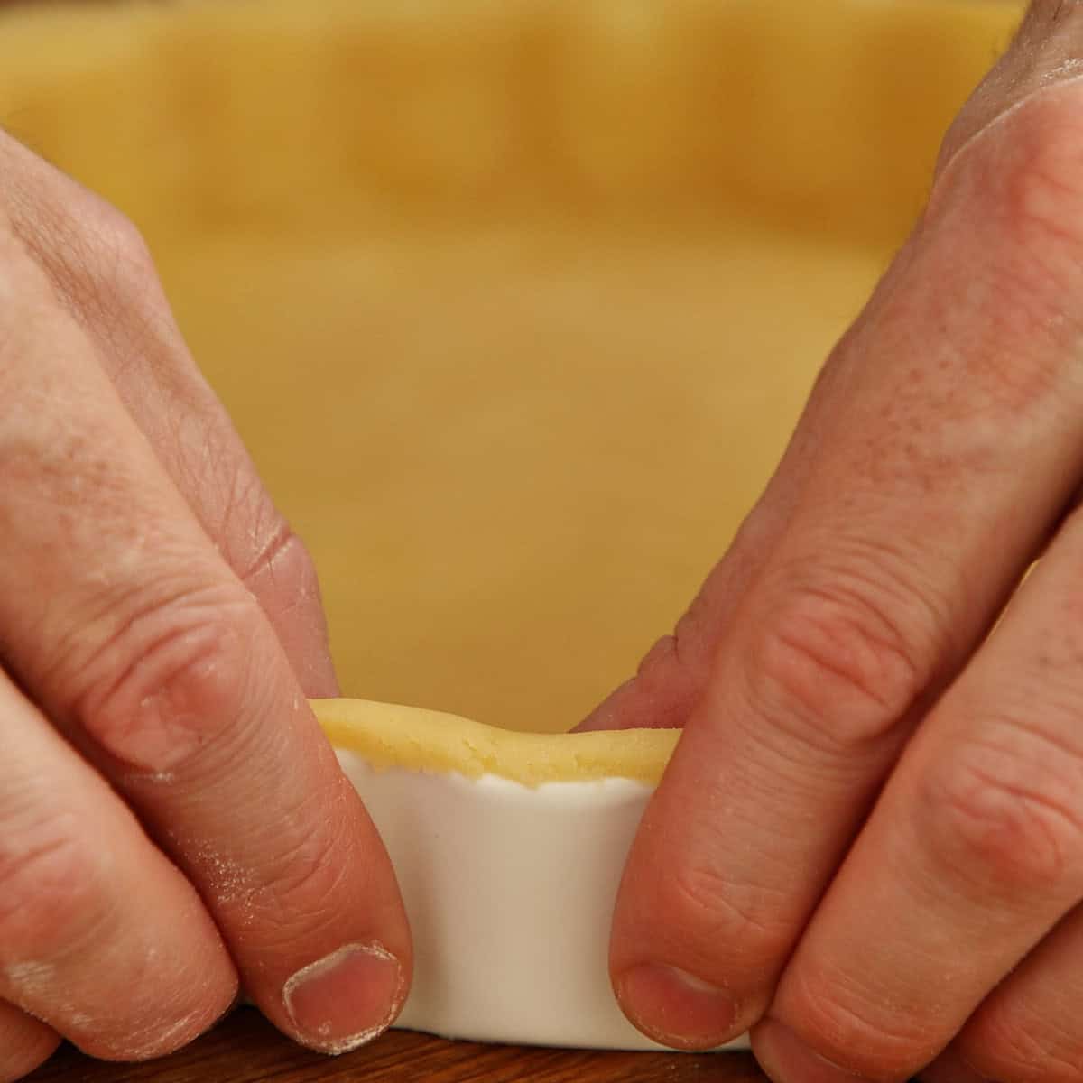 Hands stretching a thin pastry shell filled with creamy white custard filling.