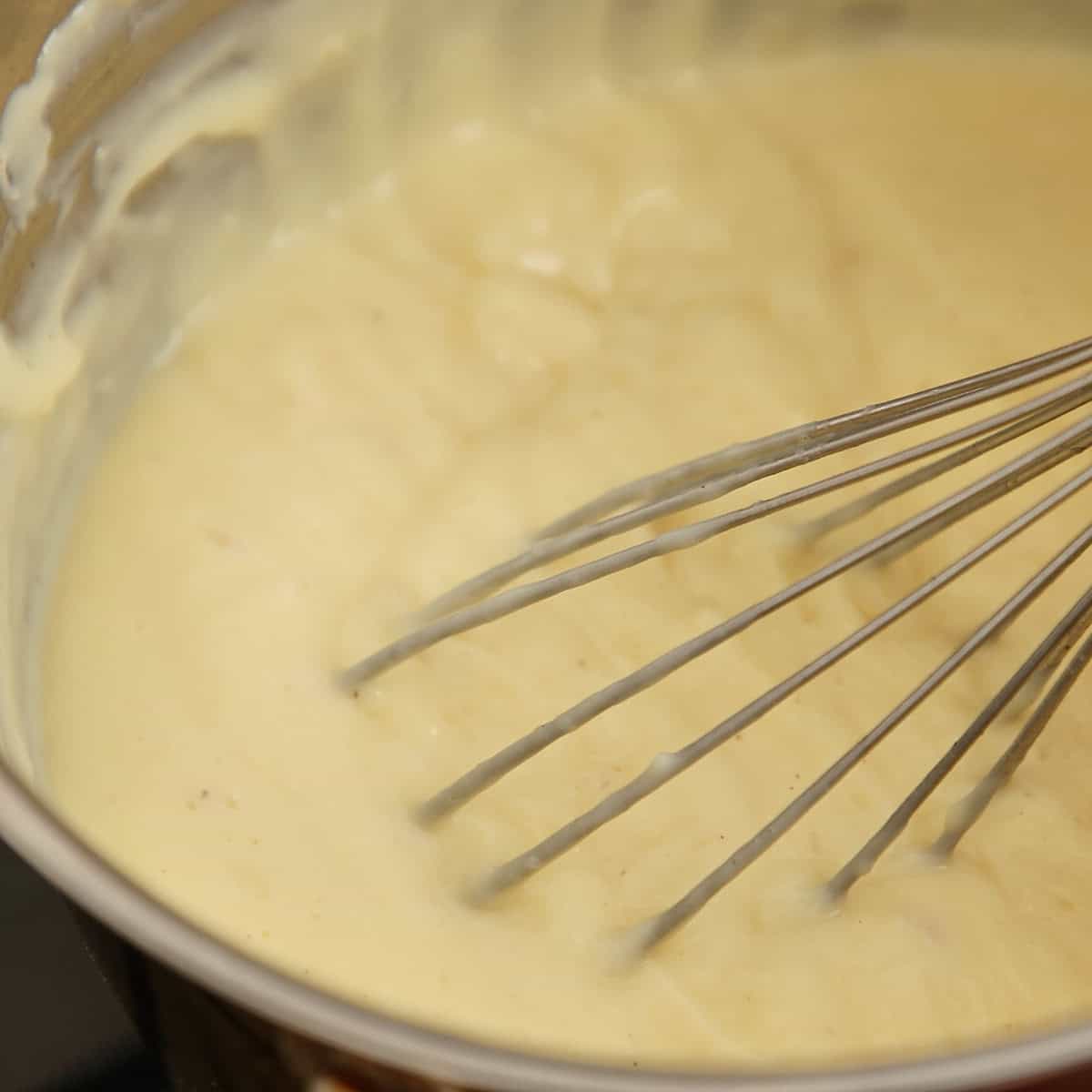 Whisk resting in a pale custard mixture in a metal sauce pan.