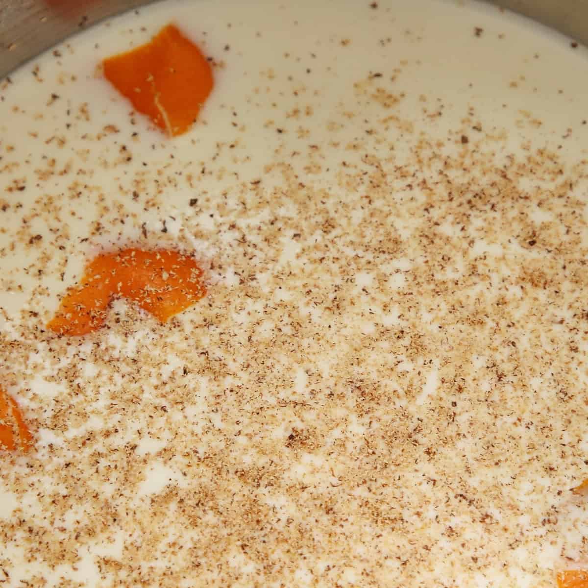 Milk, naartjie peel and nutmeg in a metal sauce pan.