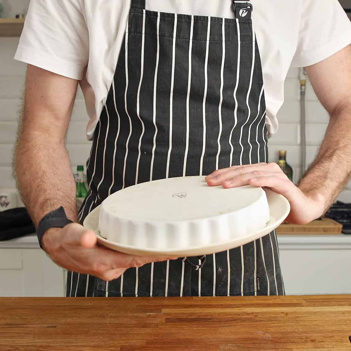Chef holding a ceramic tart dish with fluted edges and white plate.