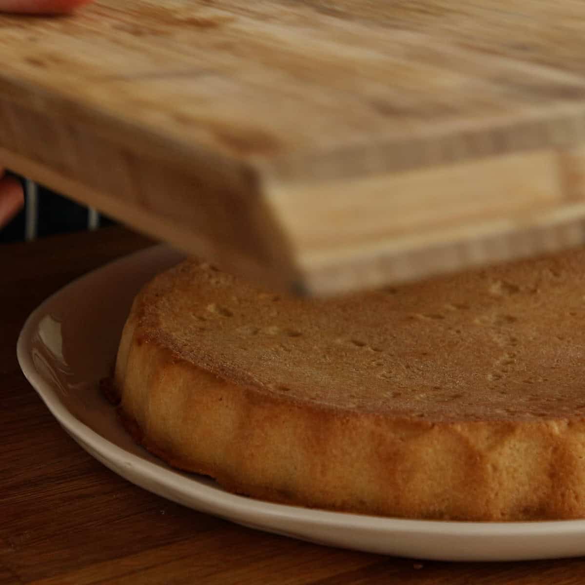Baked milk tart upside down on a plate ready for flipping onto a wooden board.