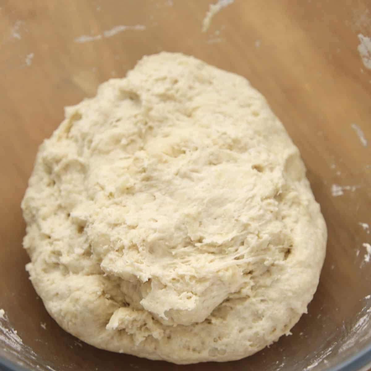 Roughly mixed naan dough in glass bowl.