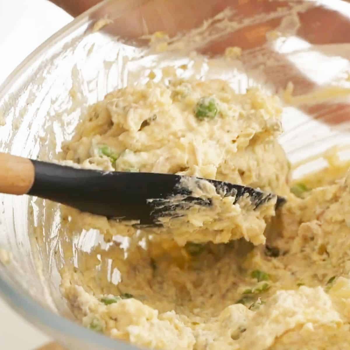 Mixing Olivieh salad gently with a spatula in a glass bowl.