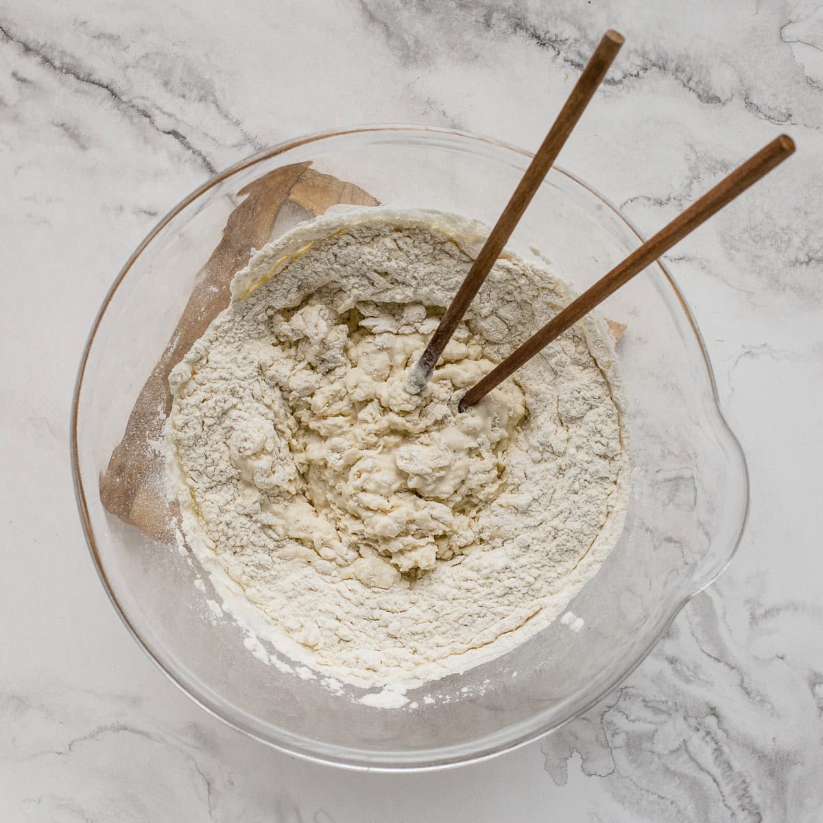 Mixing flour, sourdough starter, and water in a glass bowl.