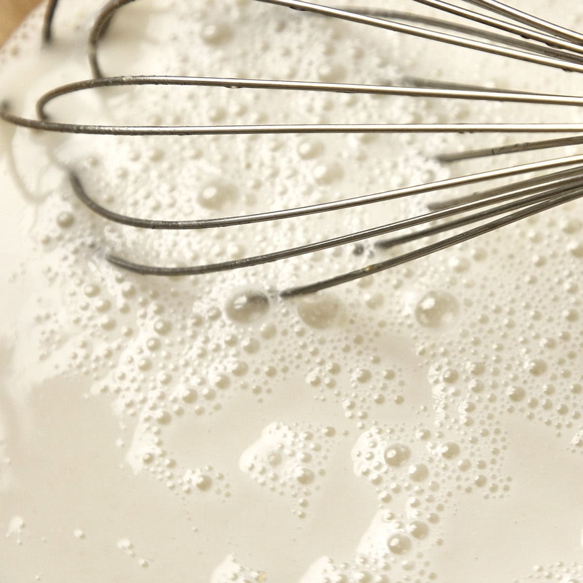 White mixture of sourdough water and salt in a bowl with a metal whisk.