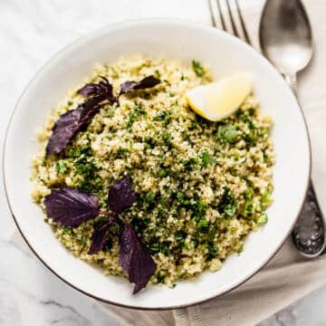 moroccan spiced couscous salad in a white bowl on marble background with purple basil and a wedge of lemon