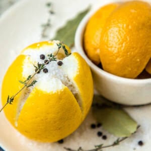 Lemon with salt, thyme, and black pepper on a plate for making preserved lemons.