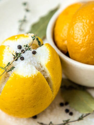 Lemon with salt, thyme, and black pepper on a plate for making preserved lemons.