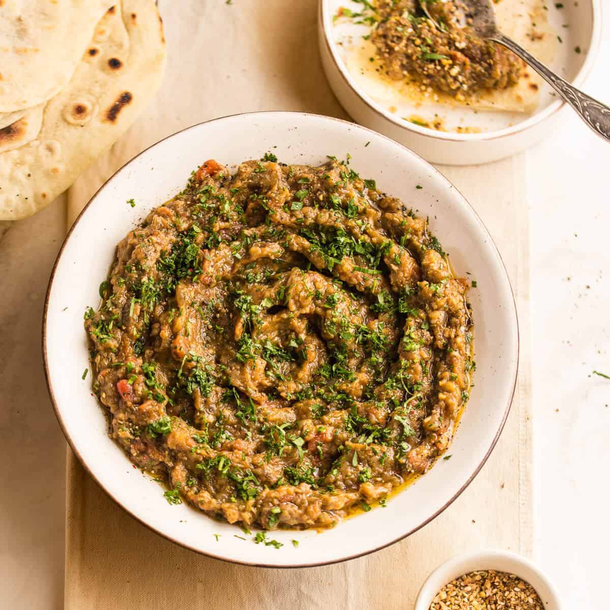 zaalouk in a white bowl on beige table cloth with flatbread.