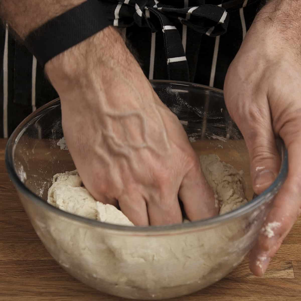 Mixing naan dough by hand in a bowl.