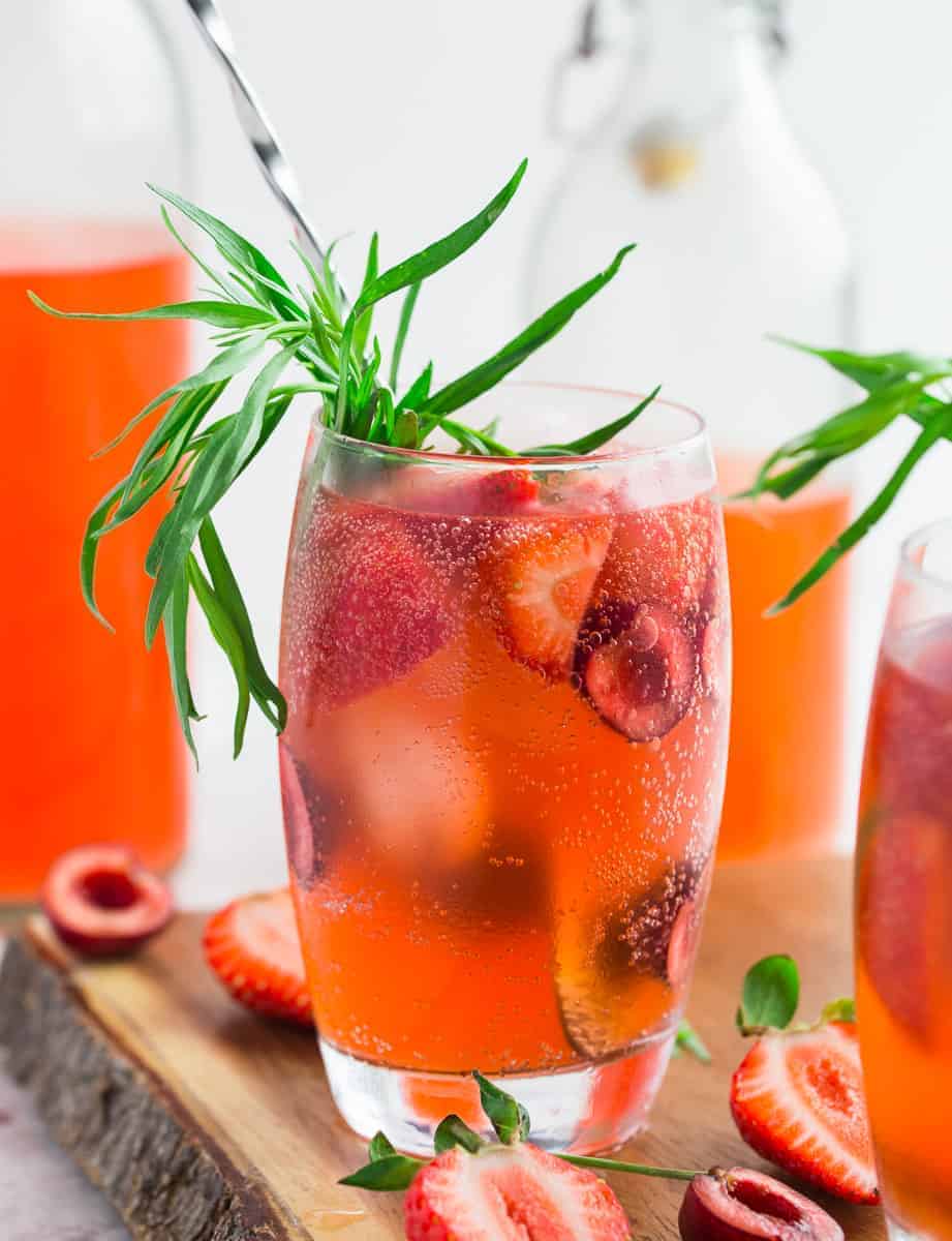 close up of strawberry soda in glass with fresh berries and tarragon on wooden board.