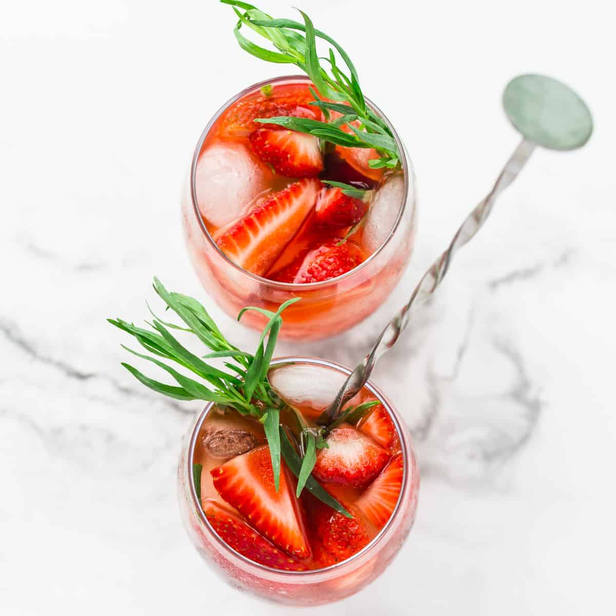 strawberry soda viewed from the top in 2 glasses with fresh berries and tarragon on marbled background.