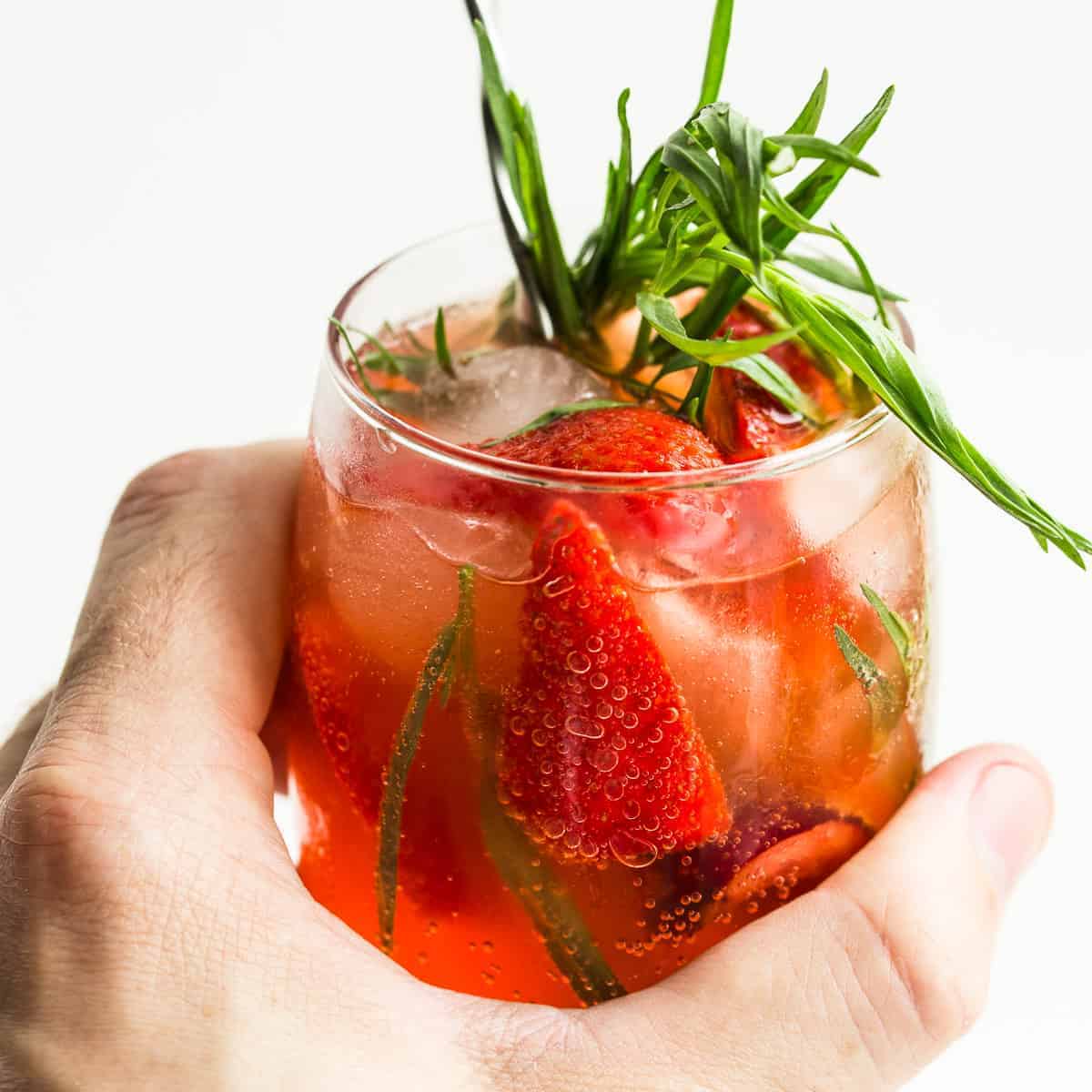 close-up of fermented strawberry soda in glass held by a hand on white background.