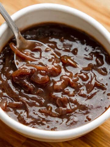Onion gravy in a white bowl on a wooden table.