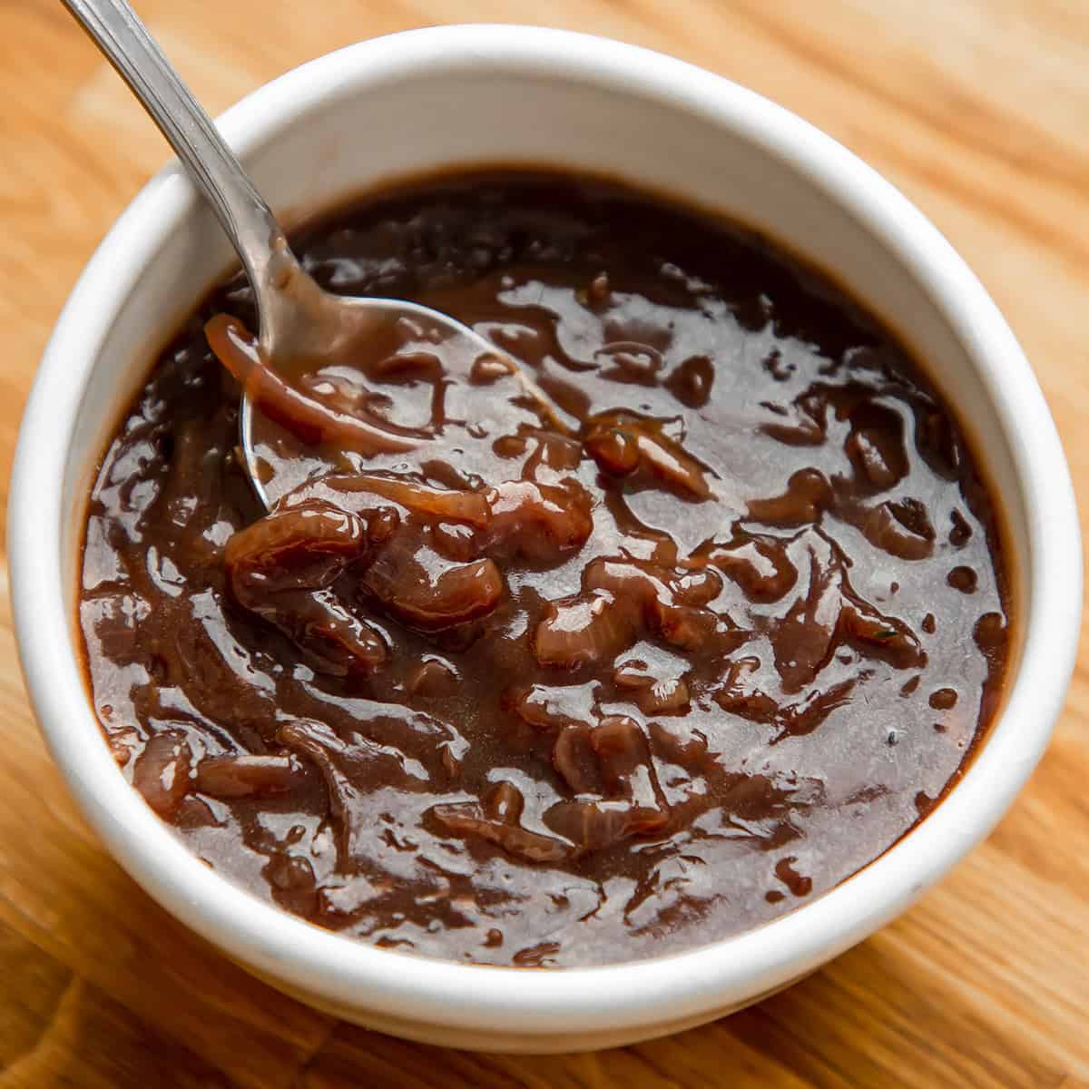 Onion gravy in a white bowl on a wooden table.
