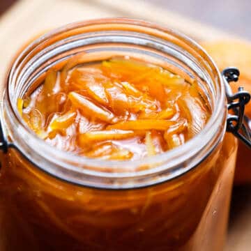 Orange marmalade in glass jar on wooden board.