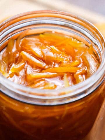 Orange marmalade in glass jar on wooden board.