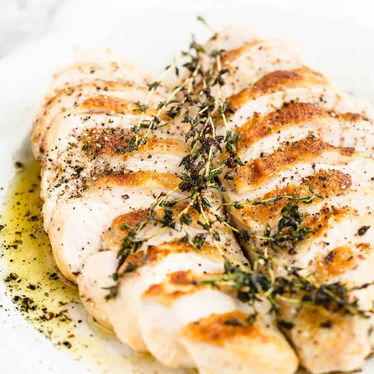 sliced oven roasted chicken breast with thyme butter on a white plate