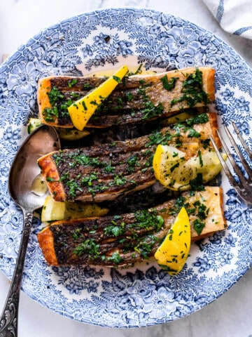 pan fried salmon fillet with crispy skin and lemon herb butter on a blue vintage plate.