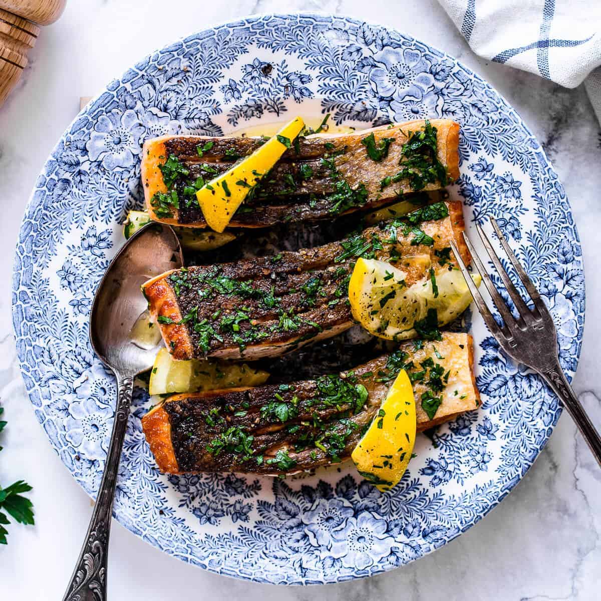 pan fried salmon fillet with crispy skin and lemon herb butter on a blue vintage plate.